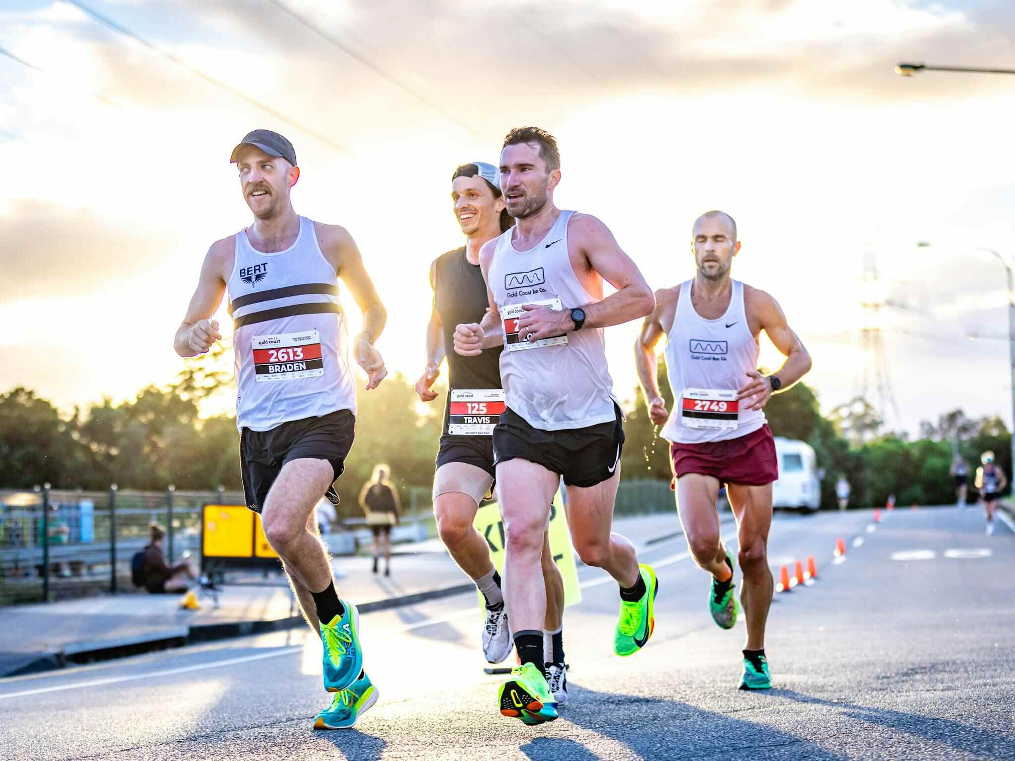gold coast events runners competing in a sunrise road race, with four men in bibs running along a closed street